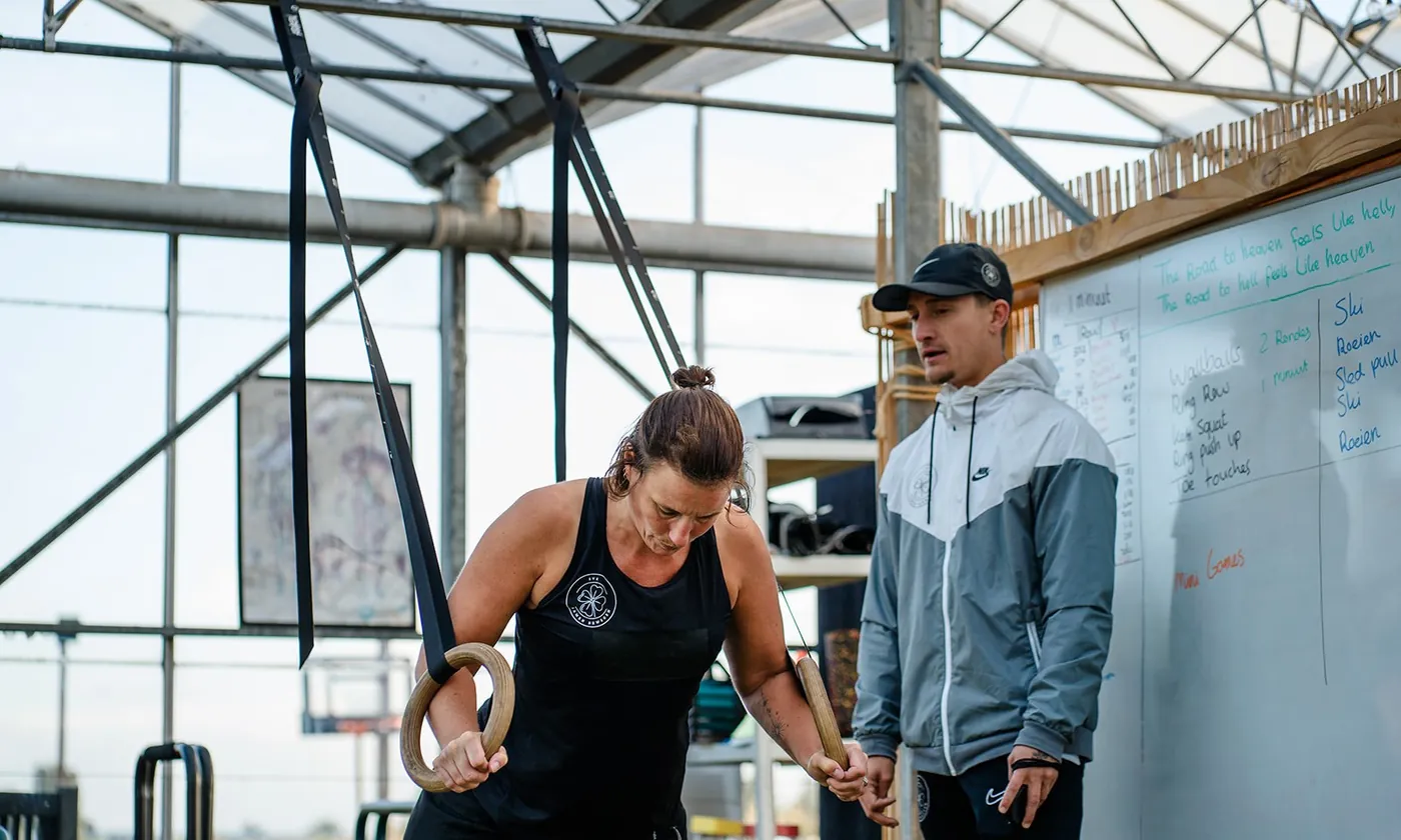 Trainer begeleidt een oefening aan de ringen